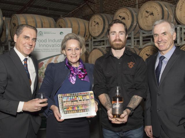 Minister holding the Premium Agrifood Market Opportunity report with three men standing in front of whiskey barrels inside Whipper Snapper Distillery.