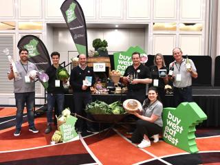 Five people standing in front a food display featuring a big green WA prop.